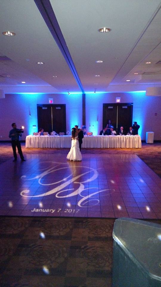 Couple dancing on a blue-lit reception floor with a custom monogram