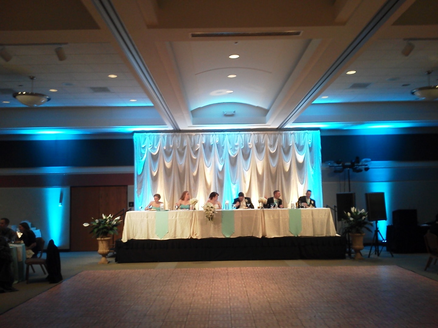 Wedding head table with turquoise uplighting and draped backdrop